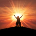 3D render of a silhouette of a female in a wheelchair with her arms raised against a sunset ocean
